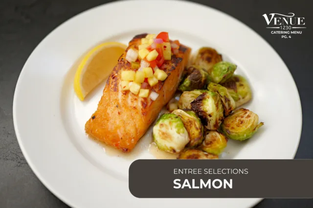 Salmon fillet topped with pineapple salsa, served with roasted Brussels sprouts and a lemon wedge on a white plate.